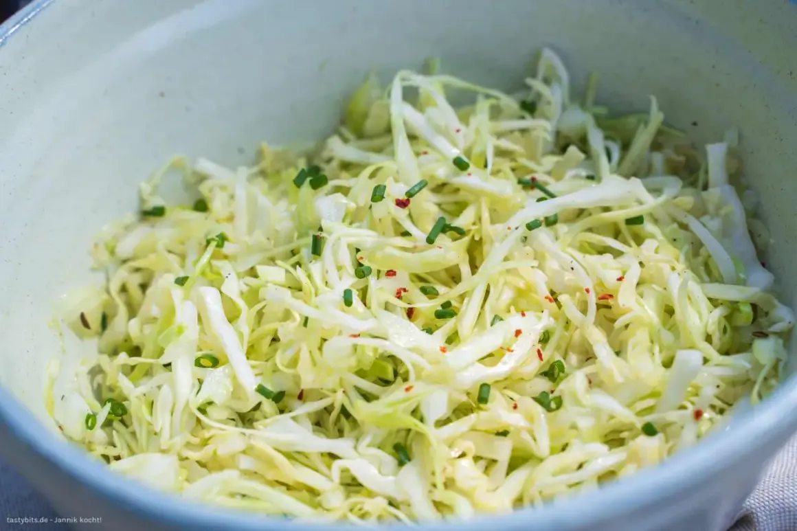 Frischer Spitzkohl Salat, fein geschnitten und mit Schnittlauch und Chiliflocken garniert, wartet in einer Schüssel.