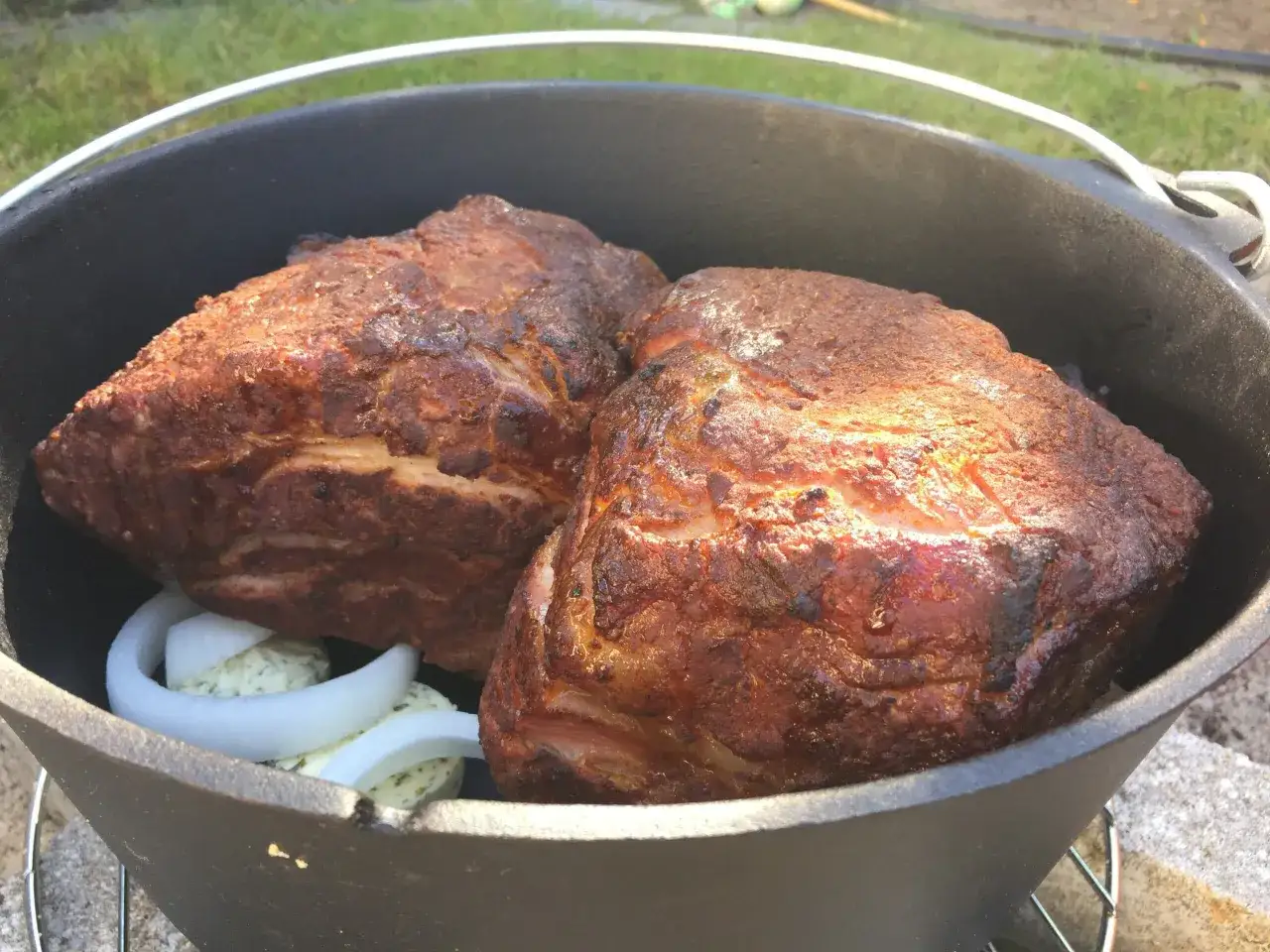 Zwei saftige Schweinebraten im Dutch Oven, bereit für Pulled Pork. Zwiebelringe und Kräuterbutter liegen daneben.