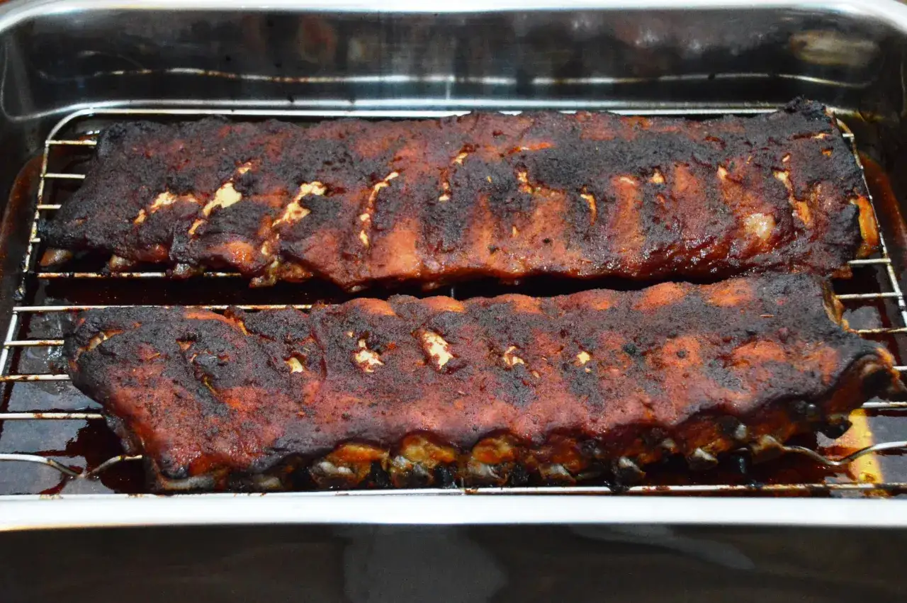 Zwei Reihen saftiger spareribs im backofen, mit einer dunklen, karamellisierten Kruste, die auf einem Rost in einer Bratenform liegen.