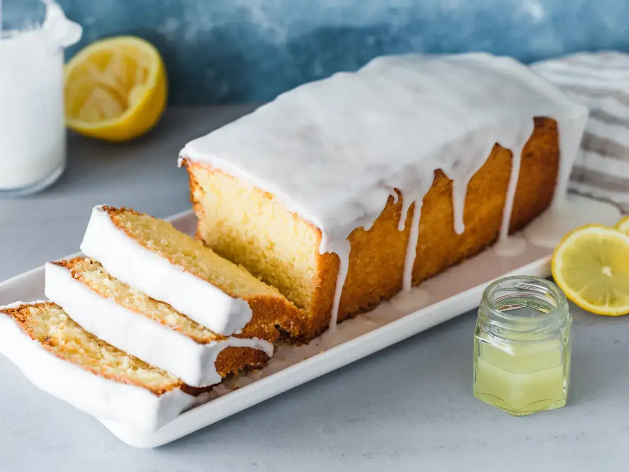 Saftiger Zitronenkuchen mit Zuckerguss, perfekt für ein Zitronenkuchen Rezept. Dazu frische Zitronenscheiben und ein Glas Zitronensaft.
