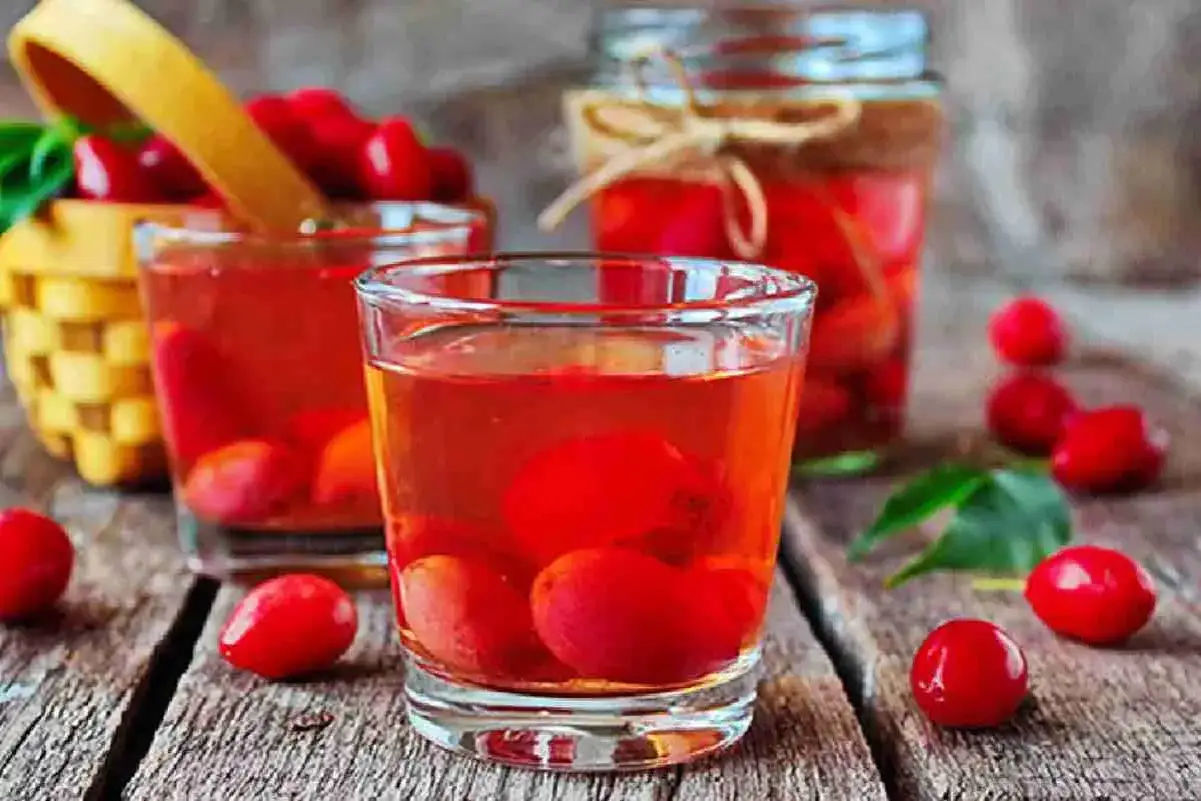 Kornelkirsche Rezepte: Rote Früchte in Gläsern und einem Glas mit Sirup, daneben ein Körbchen voller Kornelkirschen.
