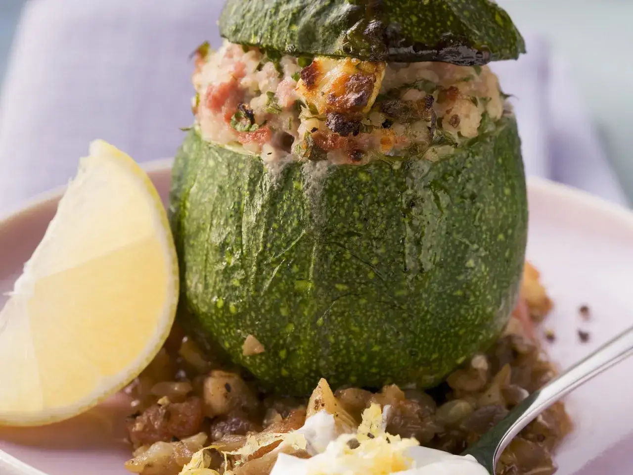 Gef&uuml;llte, runde Zucchini mit einer herzhaften Mischung aus Reis und Fleisch, serviert mit einer Zitronenspalte und Linsen.