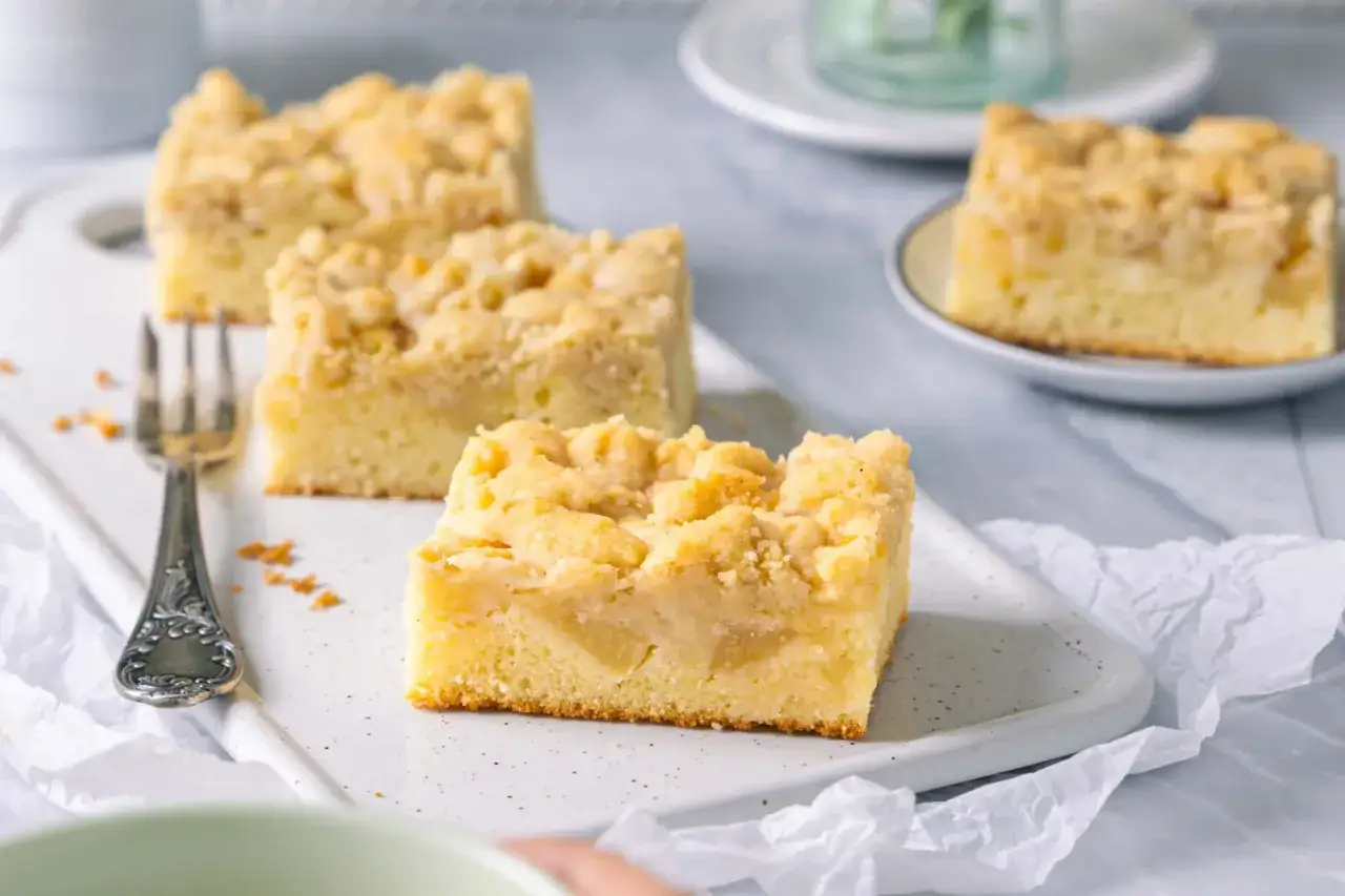 Saftiger Apfelkuchen mit Streuseln, serviert auf einem weißen Brett mit einer Gabel.