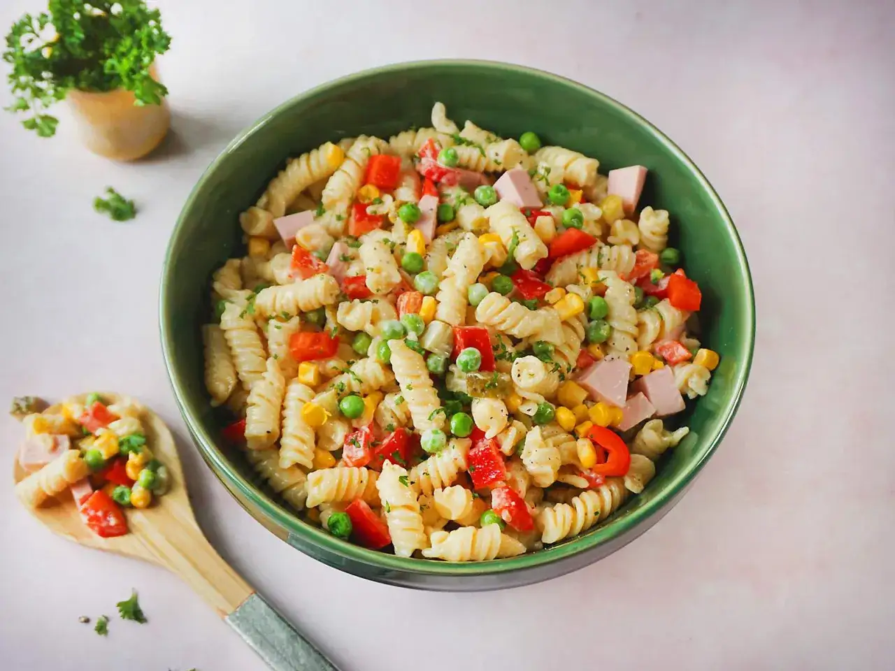 Ein köstliches nudelsalat rezept mit Spiralnudeln, Erbsen, Mais, Paprika und Schinkenwürfeln, garniert mit Petersilie.