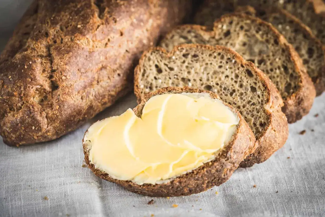 Ein rustikales Keto Brot Rezept, perfekt für Frühstück oder Snack. Eine Scheibe ist mit Butter bestrichen, daneben liegen weitere Scheiben.