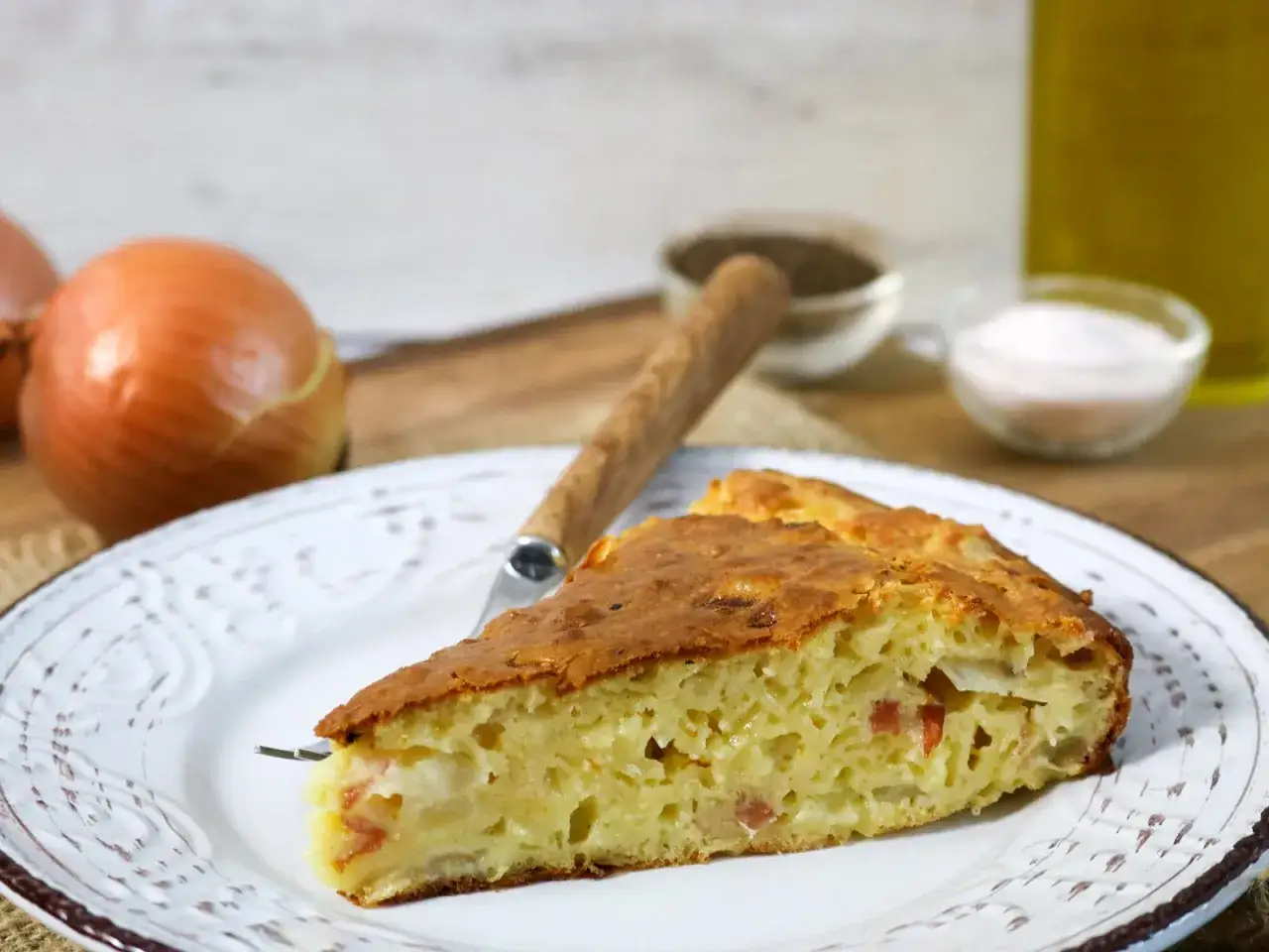 Ein St&uuml;ck herzhafter Zwiebelkuchen ohne Boden, mit Zwiebeln und Speck, auf einem Teller mit Gabel.