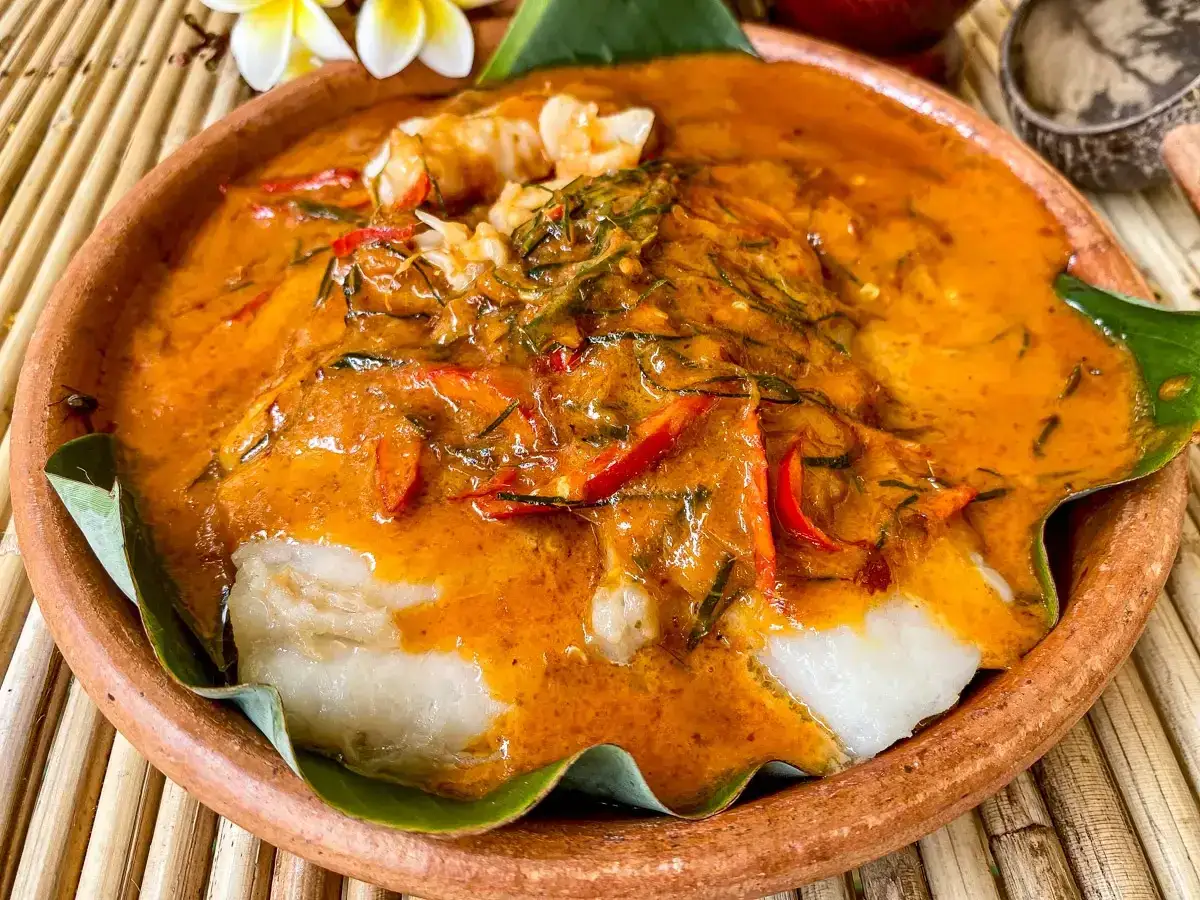 Ein köstlicher, cremiger thai curry mit Fisch und roten Chilis in einer Tonschale, garniert mit Kräutern und Blättern.