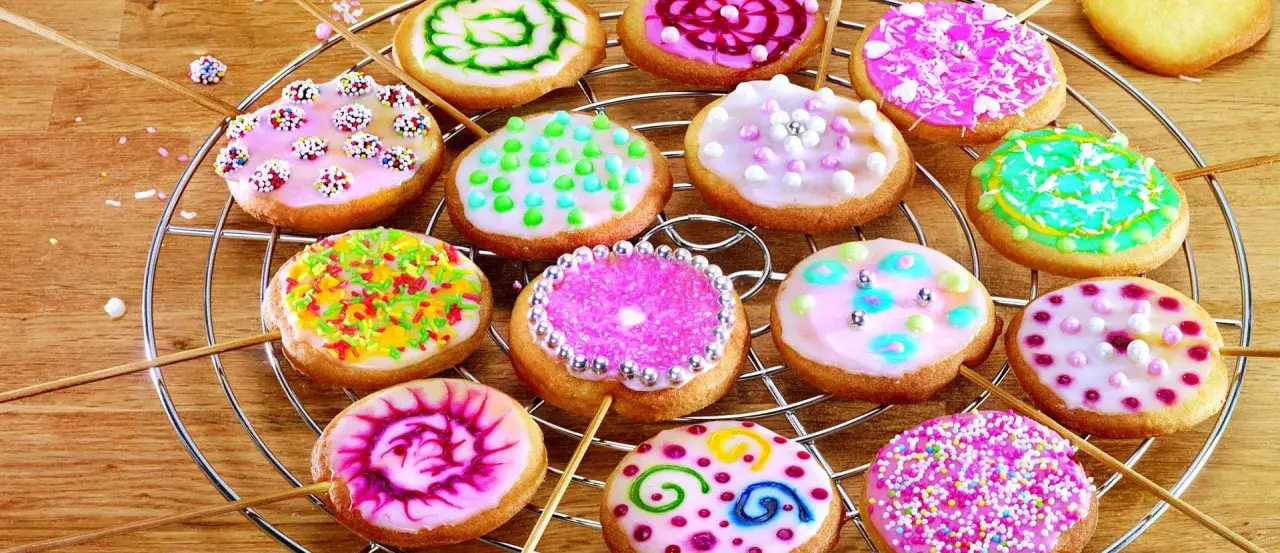 Bunte Kekse mit Zuckerguss-Rezept, verziert mit Streuseln und Perlen, auf einem Gitter.