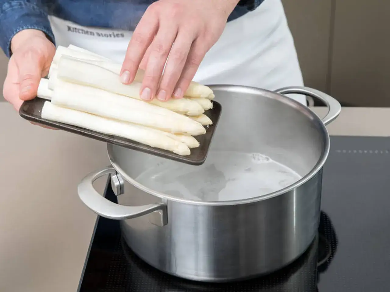 Frischer weißer Spargel wird in kochendes Wasser gegeben. So beginnt das Spargel kochen mit oder ohne Deckel.