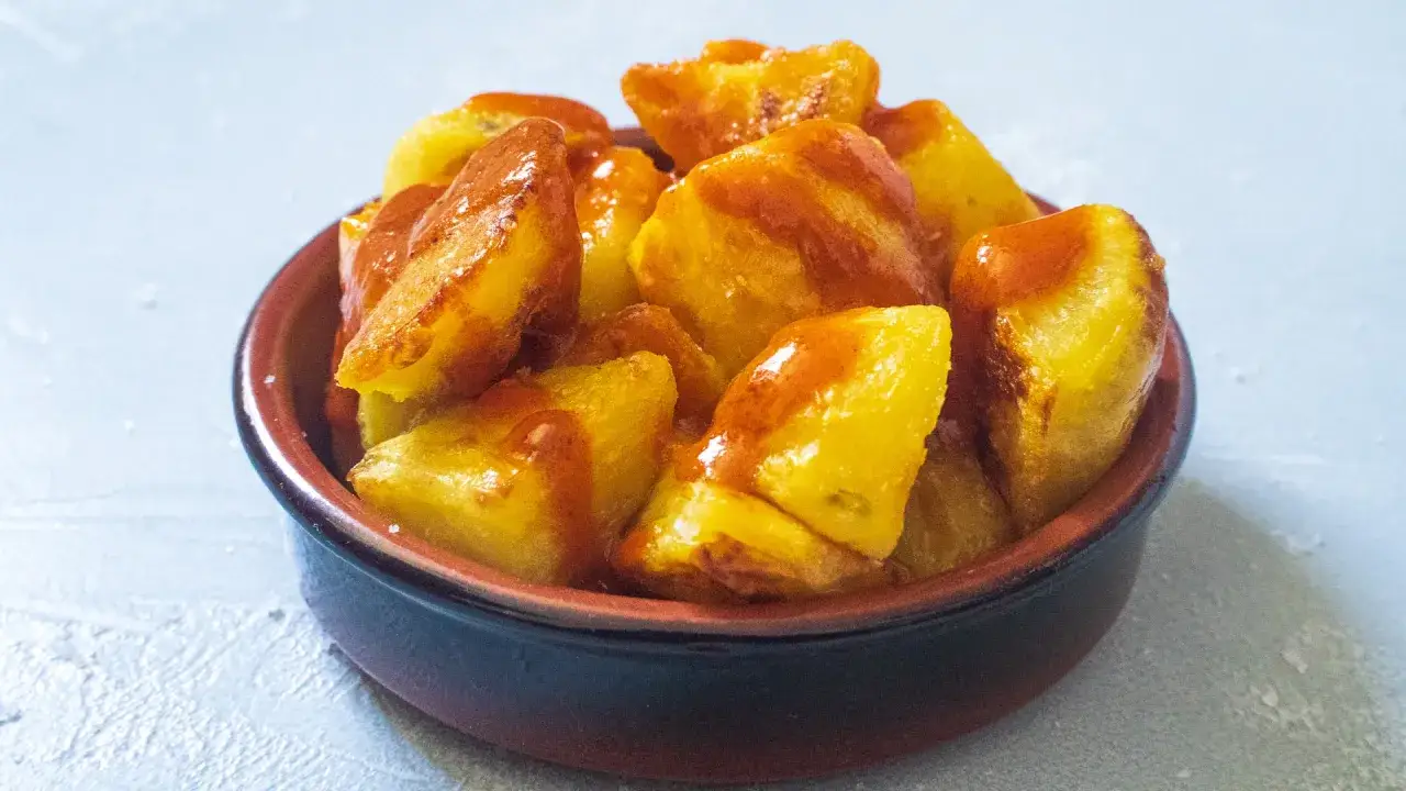 Knusprige, goldbraune Kartoffelst&uuml;cke, &uuml;bergossen mit einer w&uuml;rzigen Sauce, serviert in einer Tonschale. Ein Klassiker: Patatas Bravas.