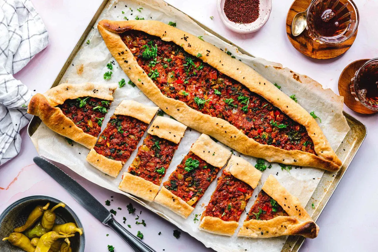 Ein k&ouml;stliches, in Scheiben geschnittenes Pide Rezept mit Hackfleischf&uuml;llung, garniert mit Petersilie und Sesam. Dazu gibt es eingelegte Peperoni und Tee.