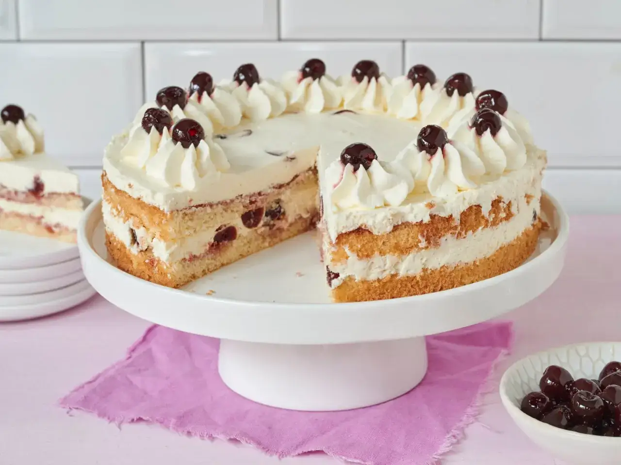 Saftiger Kuchen mit Sahne und Kirschen, perfekt zum Amarenakirschen selber machen. Ein St&uuml;ck fehlt, daneben eine Schale mit Kirschen.