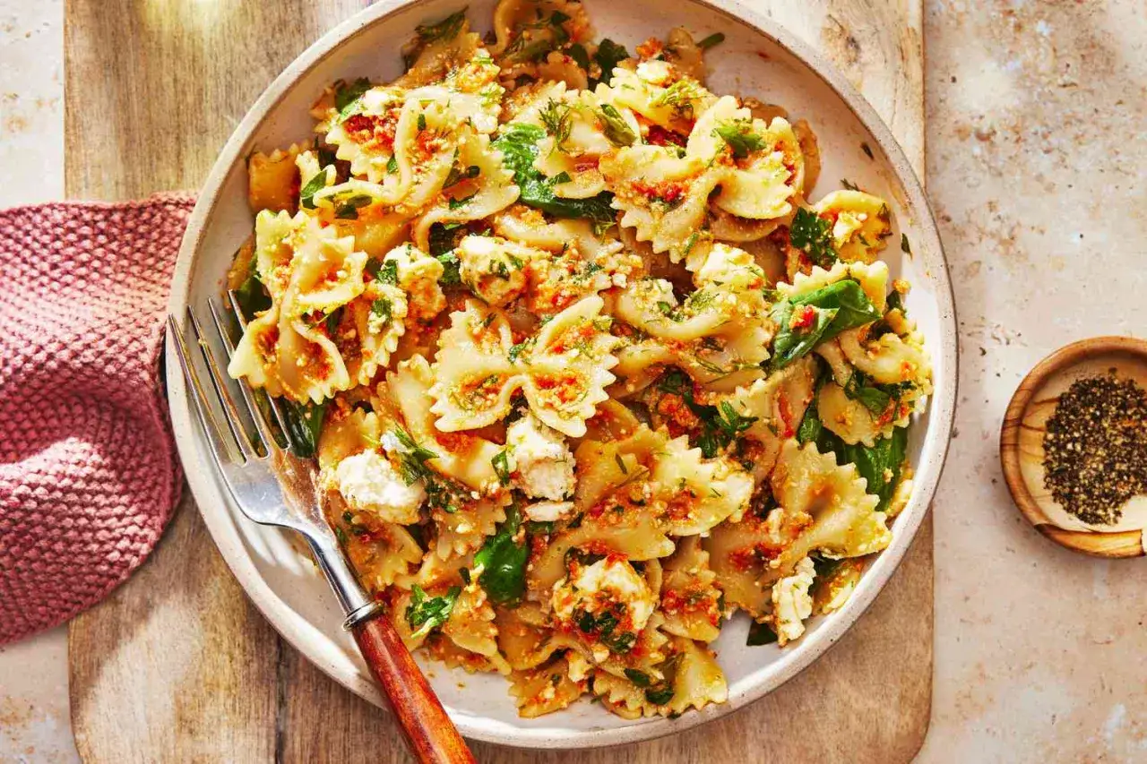 Farfalle-Nudelsalat mit getrockneten Tomaten, Feta und frischen Kr&auml;utern, serviert in einer Sch&uuml;ssel mit einer Gabel.