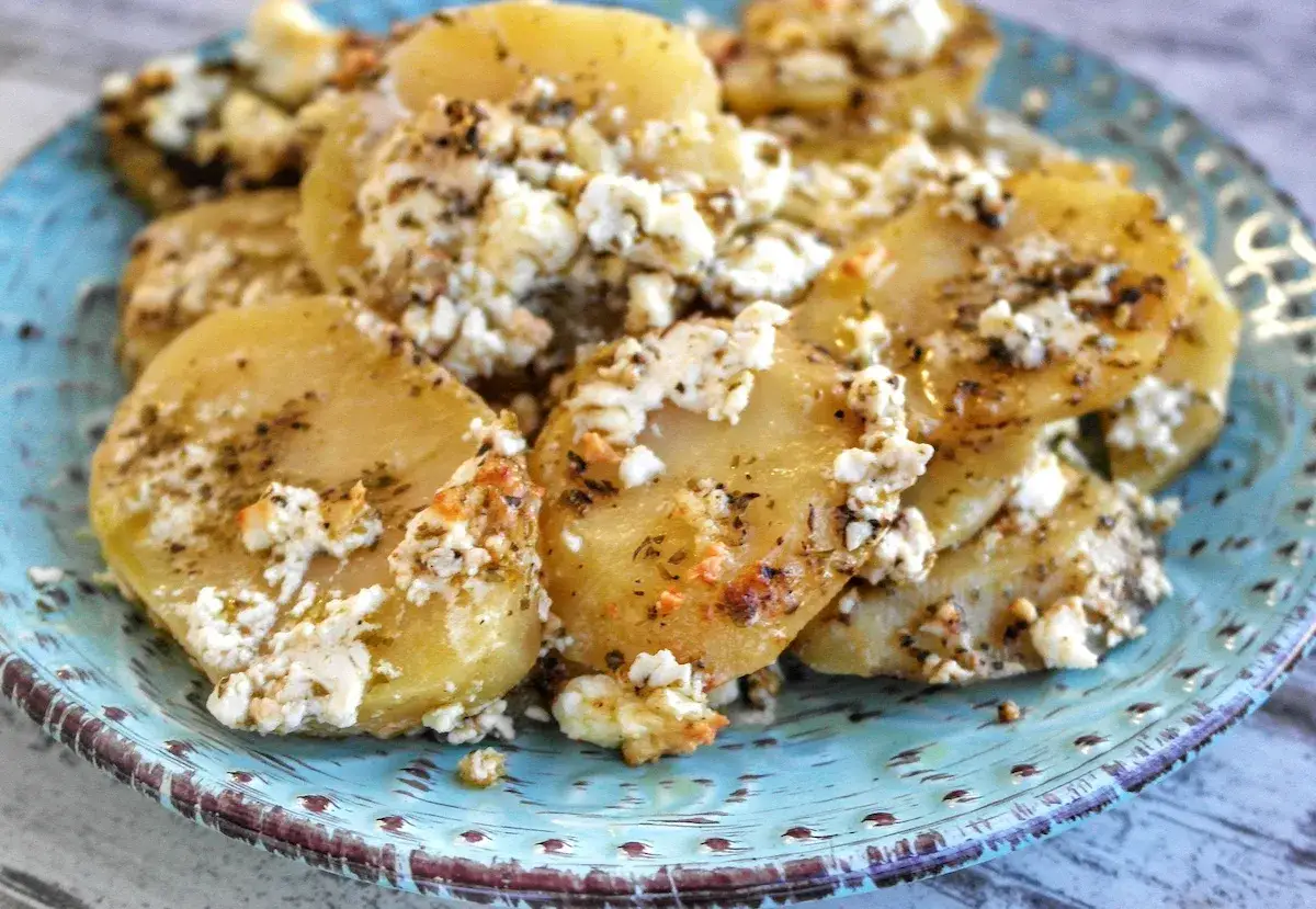 Gebackene Kartoffelscheiben mit zerbr&ouml;seltem Feta und Kr&auml;utern auf einem blauen Teller. Ein leckeres Gericht f&uuml;r Feta Rezepte.