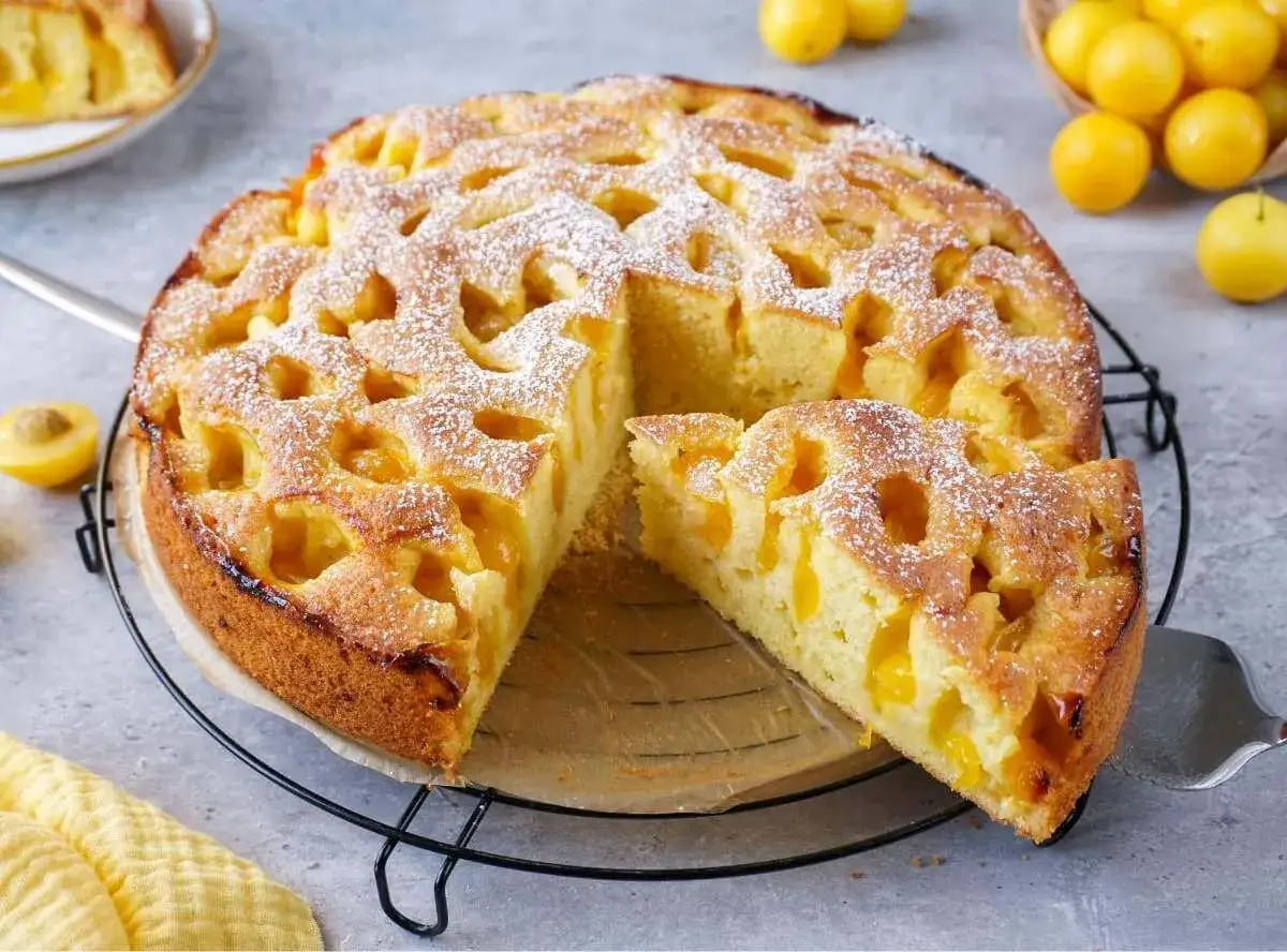 Ein goldbrauner mirabellen kuchen, mit Puderzucker bestäubt, wartet auf seine Genießer. Ein Stück ist bereits herausgeschnitten.