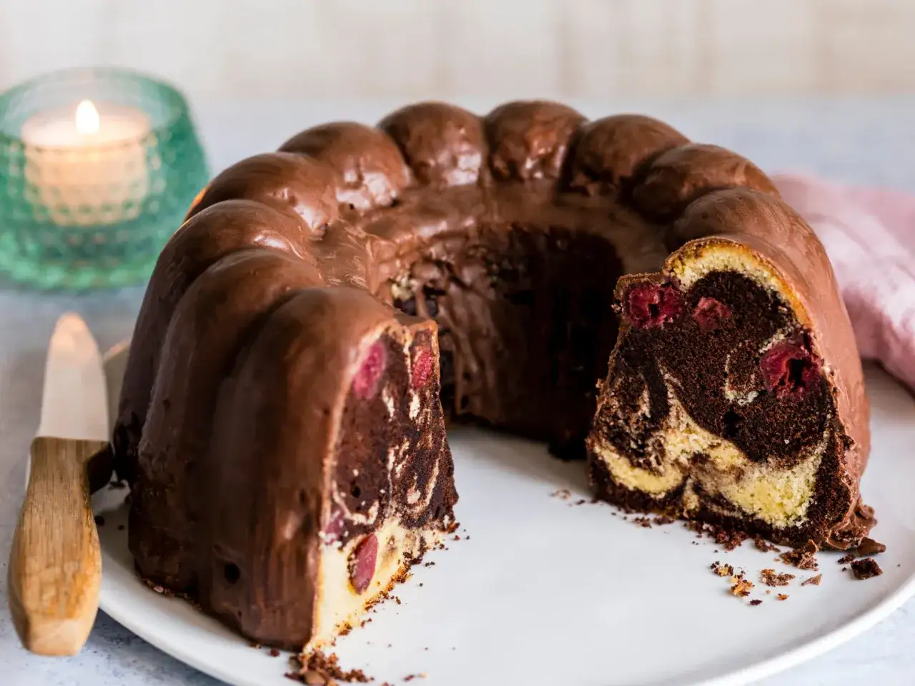 Ein saftiger Marmorkuchen mit Kirschen, überzogen mit Schokoladenglasur, auf einem weißen Teller.