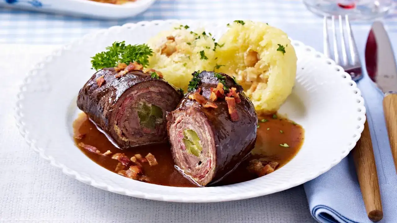 Zwei Rouladen im Schnellkochtopf, serviert mit Klößen und dunkler Soße, garniert mit Speck und Petersilie.
