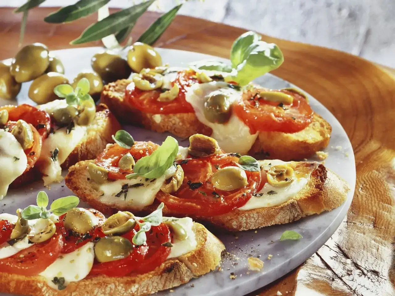 Bruschetta mit Tomate, Mozzarella und Oliven, garniert mit frischem Basilikum. Ein köstlicher Snack, der Lust auf mehr macht.