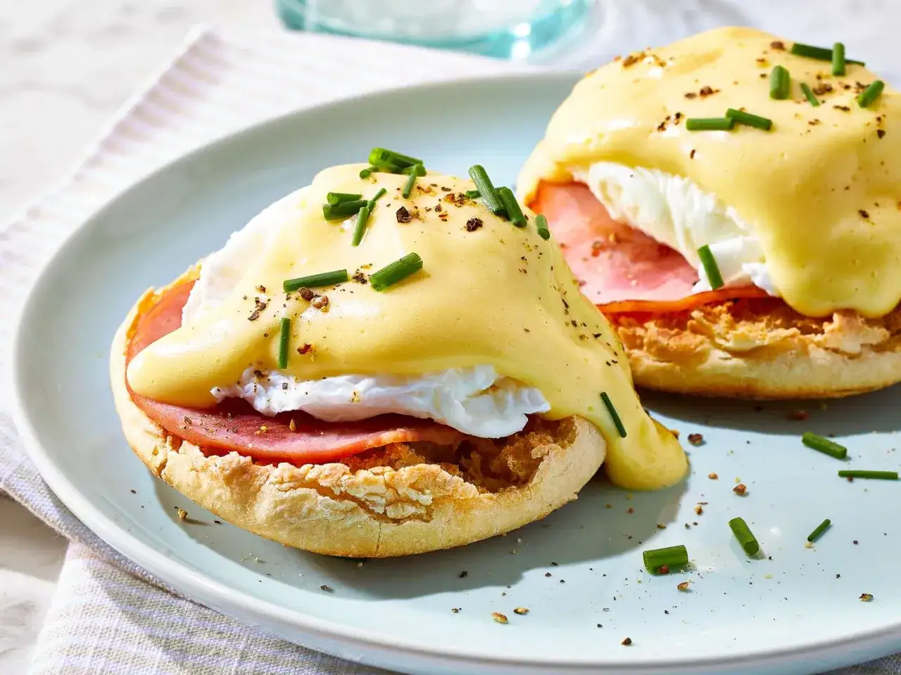 Zwei köstliche Eggs Benedict auf einem Teller, mit pochiertem Ei, Schinken und cremiger Sauce Hollandaise, bestreut mit Schnittlauch.
