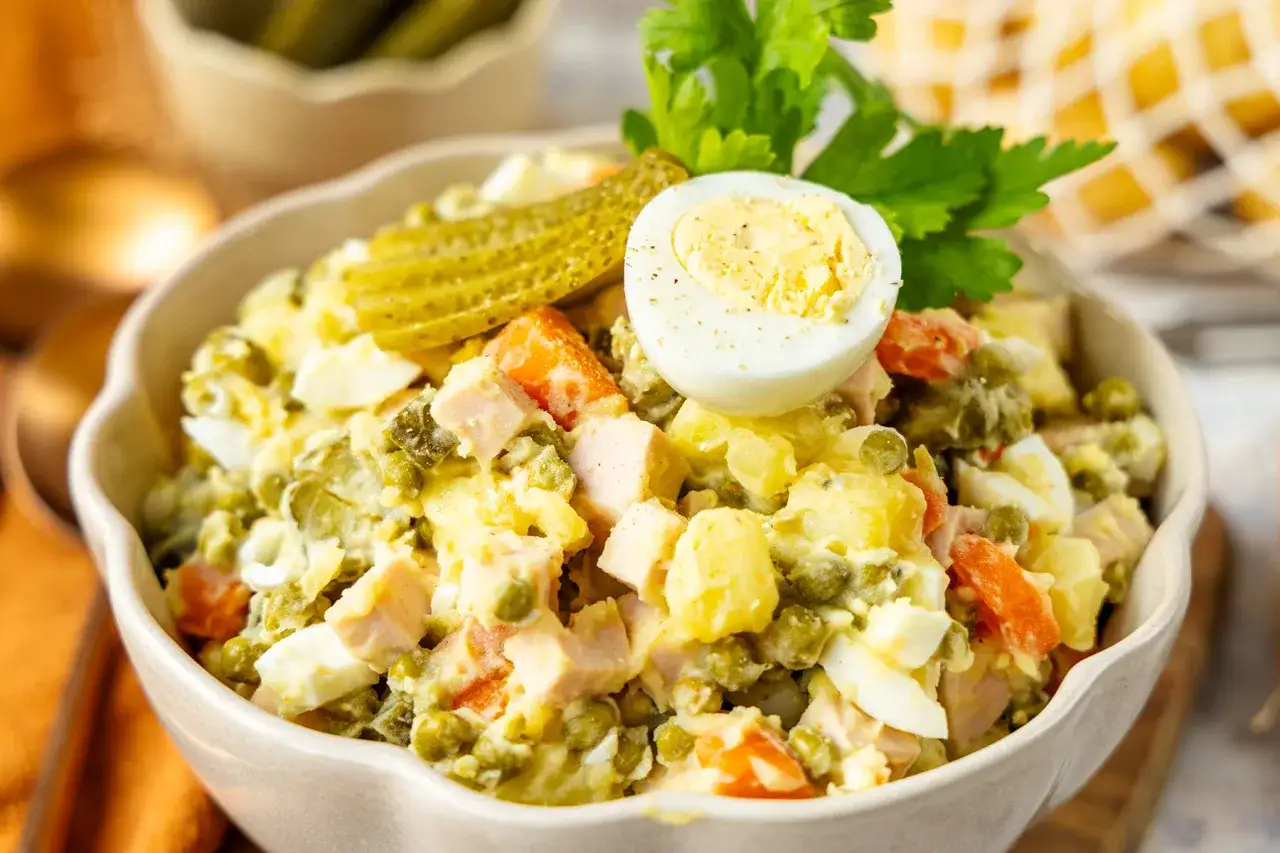 Ein cremiger Olivier Salat mit Erbsen, Karotten, Eiern und Gew&uuml;rzgurken, garniert mit einer halben Eierscheibe und Petersilie.