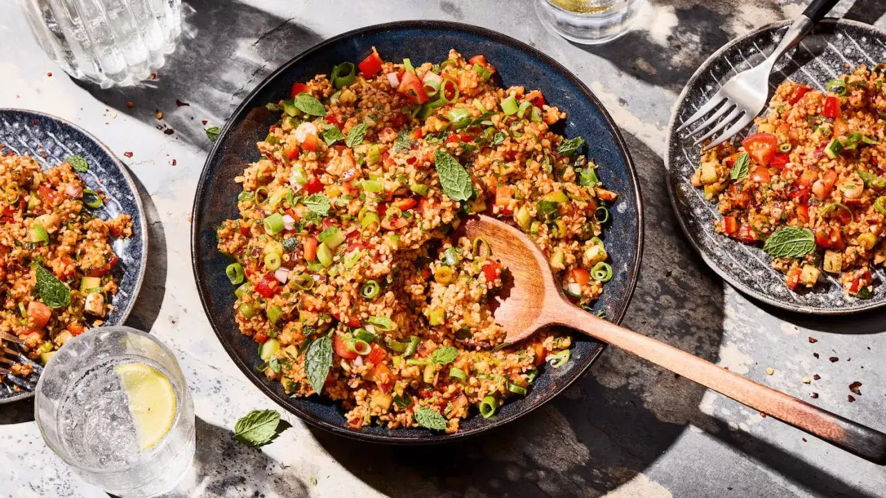 Frischer Bulgursalat mit Tomaten, Gurken, Fr&uuml;hlingszwiebeln und Minze, serviert in einer Sch&uuml;ssel und auf Tellern.