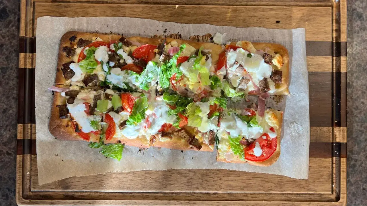 Rechteckiges griechisches Fladenbrot mit Trockenhefe, belegt mit Fleisch, Tomaten, Salat und Joghurt-Dressing.