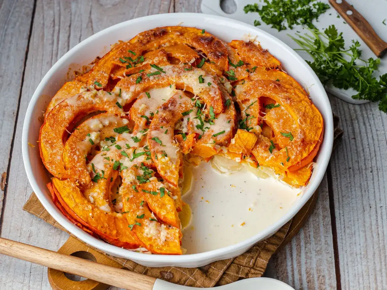 Herzhafte Hokkaido-Rezepte: Cremiger Auflauf mit geschichteten Kürbisscheiben, überbacken mit Käse und garniert mit Petersilie.