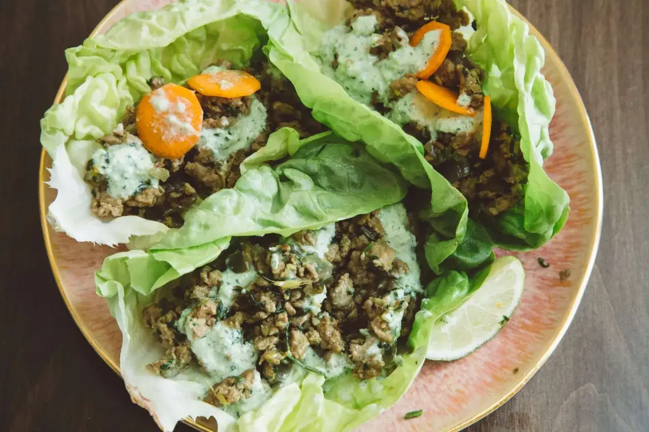 Leckeres Wraps-Rezept: Hackfleischfüllung in knackigen Salatblättern mit cremiger Sauce und Karottenstreifen.