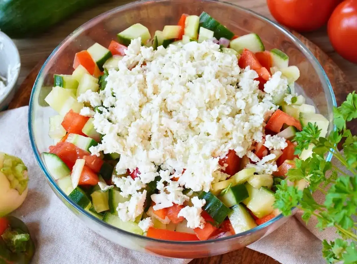 Schopska Salat in einer Glasschüssel, mit Tomaten, Gurken und viel zerbröseltem Feta-Käse garniert.