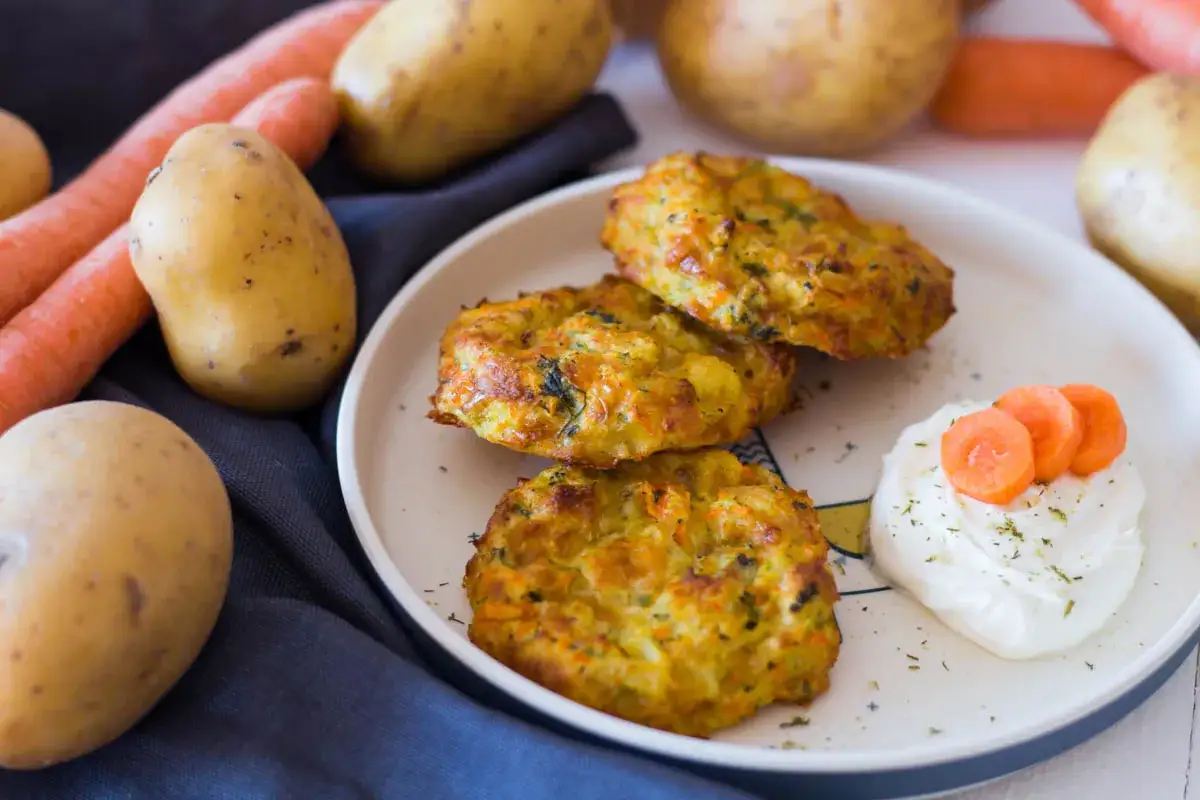 Goldbraune Kartoffelpuffer mit Karotten, serviert mit einem Klecks Dip und frischen Karottenscheiben. Köstliche Kartoffeln im Ofen zubereitet.