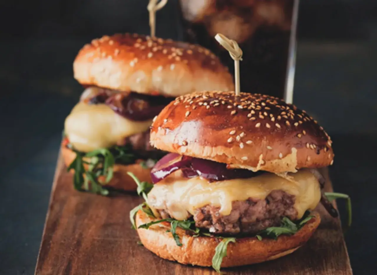 Saftige Burger mit geschmolzenem K&auml;se und roten Zwiebeln auf einem Holzbrett. Ein tolles burger buns rezept f&uuml;r jeden Anlass.