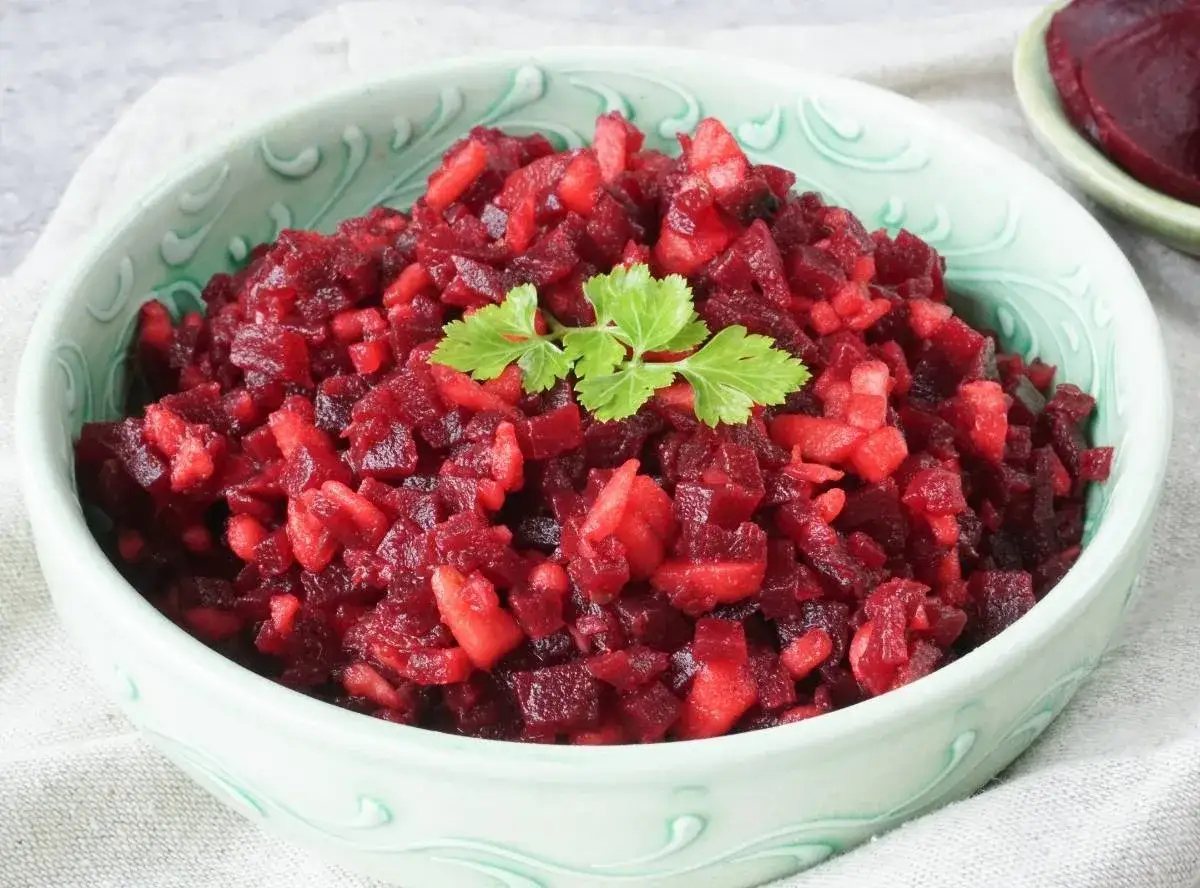 Schüssel mit leuchtend rotem Rote Bete Salat mit Apfelstücken, garniert mit einem grünen Blatt.