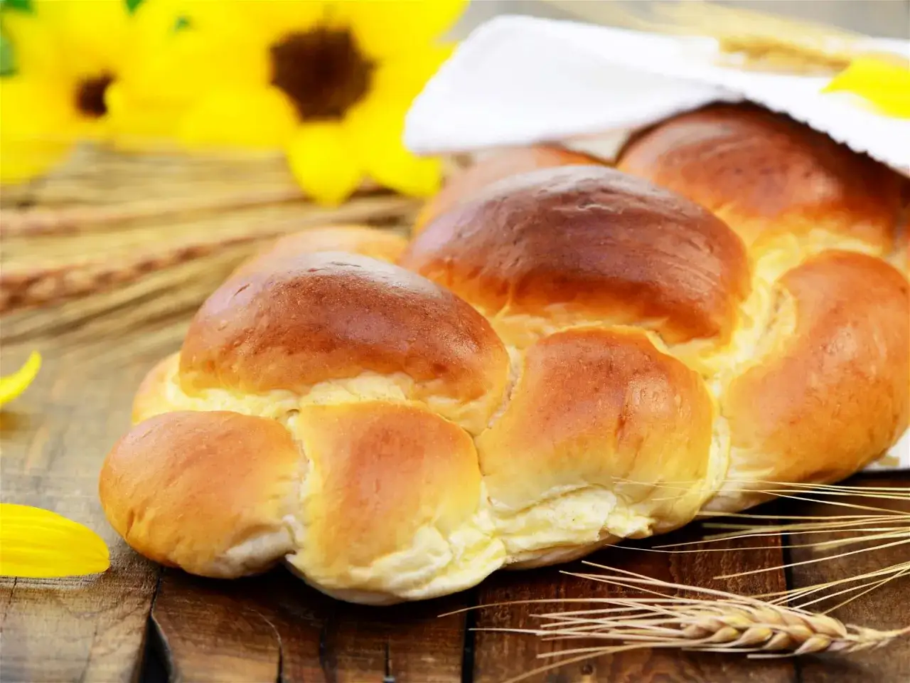 Goldbrauner Hefezopf, frisch gebacken, mit Sonnenblumen und Kornähren dekoriert. Ein leckeres Hefezopf Rezept zum Nachbacken.