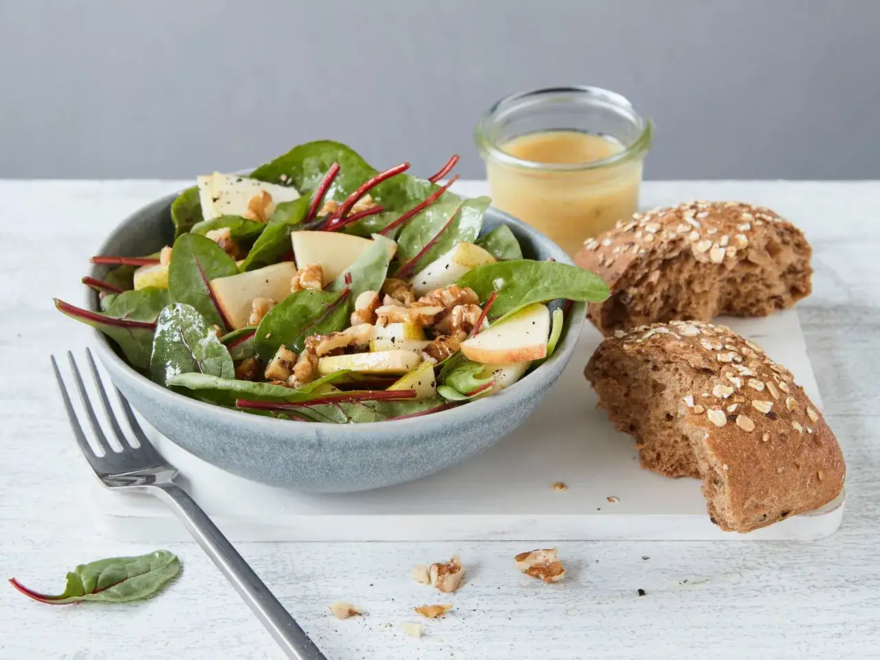 Frischer mangold salat mit Apfelstücken und Walnüssen, dazu ein Dressing und Vollkornbrötchen.