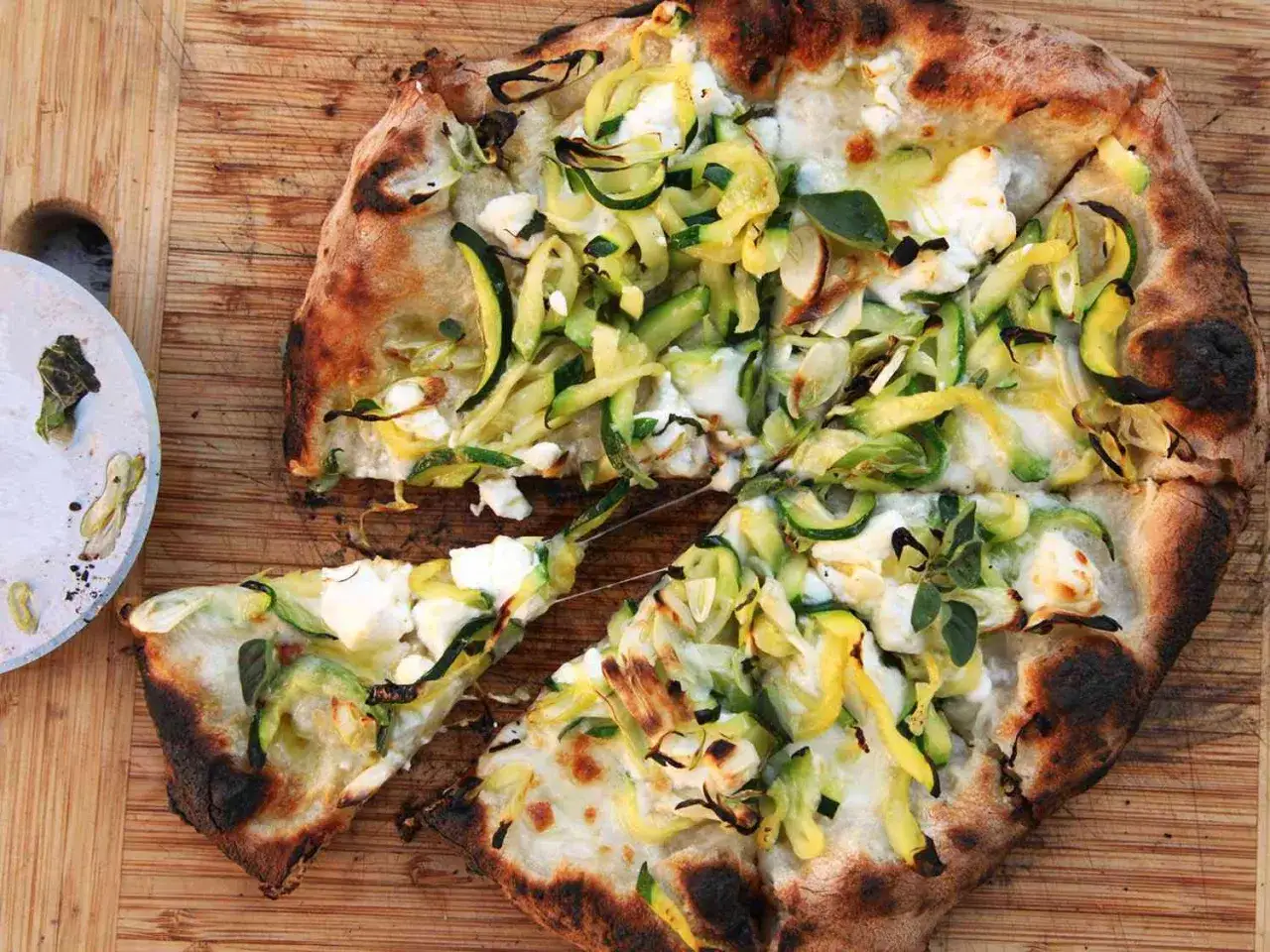 Eine köstliche Zucchini-Pizza mit viel Käse und frischen Kräutern, auf einem Holzbrett serviert.