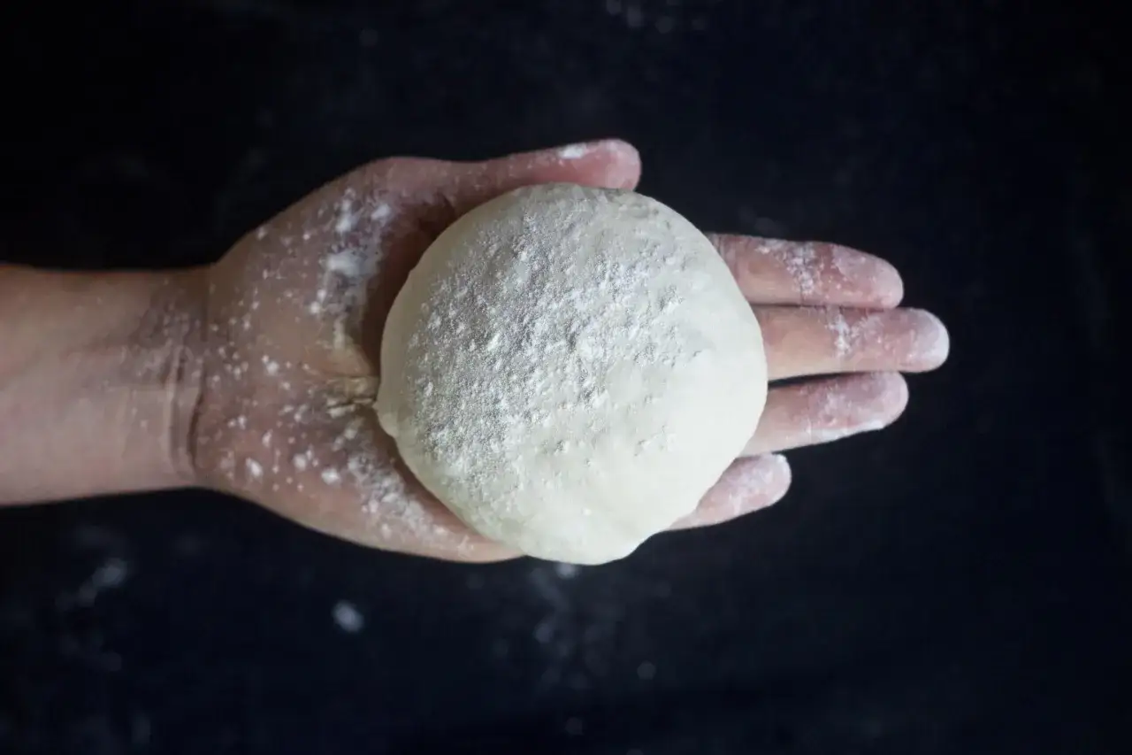 Eine Hand hält einen runden Ball aus pizzateig mit trockenhefe, bestäubt mit Mehl.