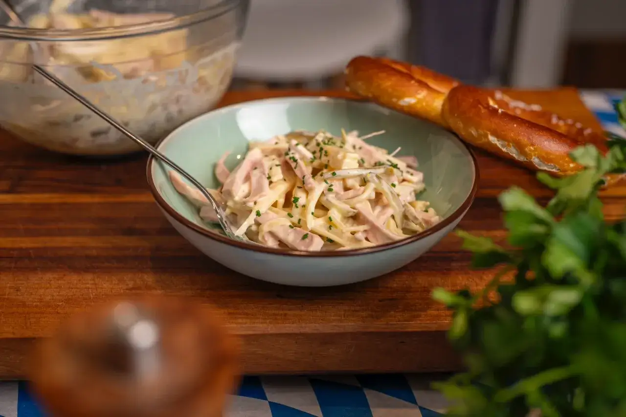 Schmackhaftes Fleischsalat Rezept mit Wurst, Gewürzgurken und Mayonnaise, garniert mit Schnittlauch. Dazu ein Brezel.