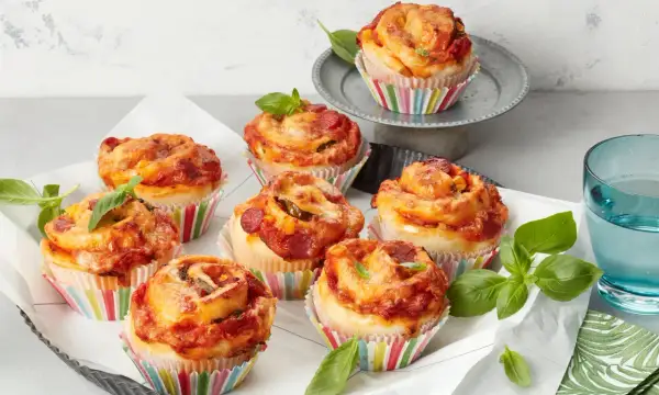 Leckere Pizza Muffins mit Salami und Käse, garniert mit frischem Basilikum.