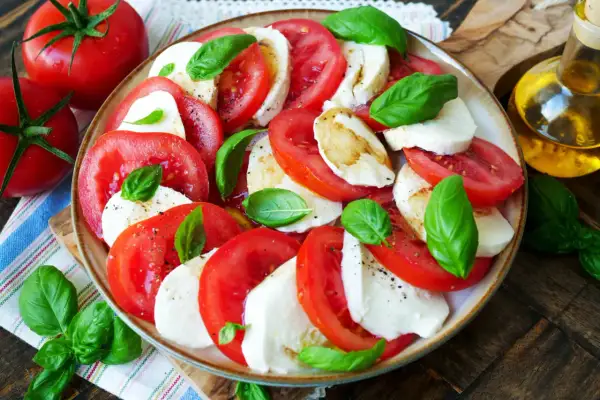 Frischer Tomate Mozzarella Salat mit Basilikum, beträufelt mit Olivenöl.