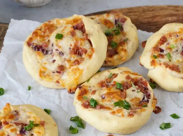 Flammkuchen Schnecken mit Speck, Käse und Frühlingszwiebeln, gebacken auf Backpapier.