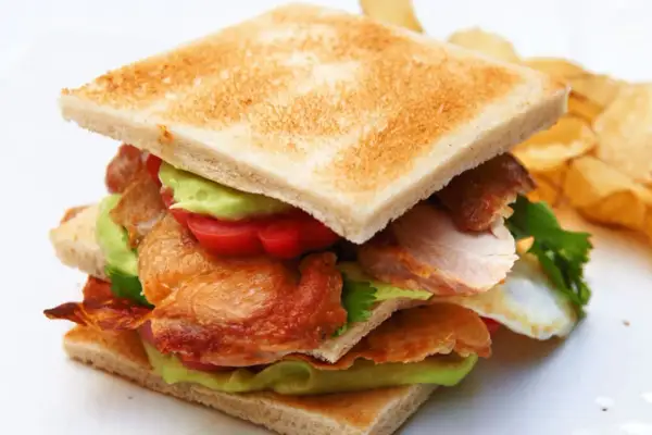Ein saftiges Club Sandwich Rezept mit Hähnchen, Avocado, Tomaten und knusprigem Speck. Dazu Kartoffelchips.