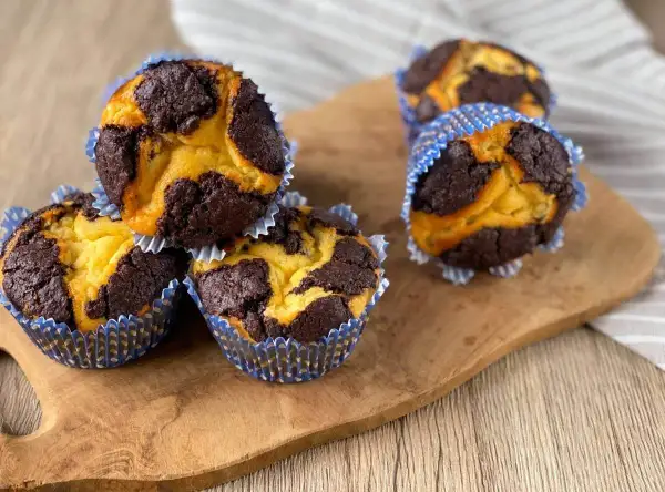Schokoladen-Vanille-Zupfkuchen-Muffins in blauen Papierförmchen auf einem Holzbrett.