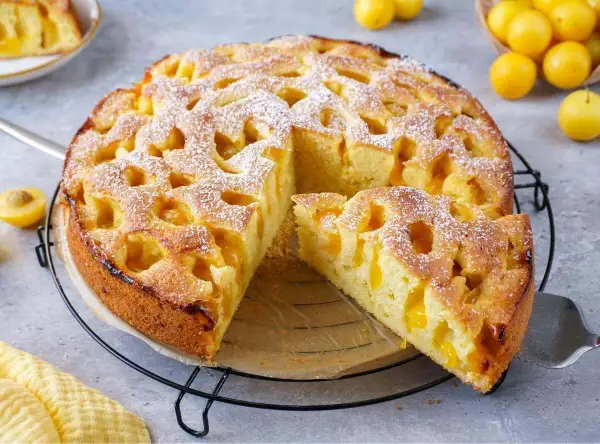 Ein goldbrauner mirabellen kuchen, mit Puderzucker bestäubt, wartet auf seine Genießer. Ein Stück ist bereits herausgeschnitten.