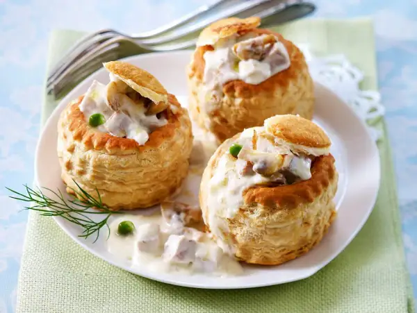 Drei Blätterteig-Schiffchen gefüllt mit cremigem Ragout Fin, garniert mit Erbsen und Dill.