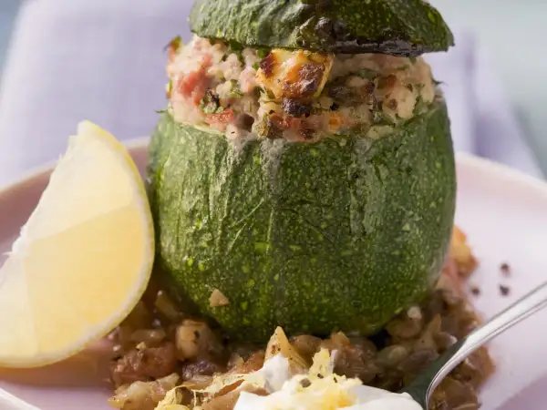 Gefüllte, runde Zucchini mit einer herzhaften Mischung aus Reis und Fleisch, serviert mit einer Zitronenspalte und Linsen.