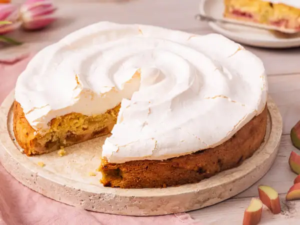 Ein köstlicher Rhabarberkuchen mit Baiser, dessen fluffige Haube leicht gebräunt ist. Ein Stück fehlt bereits.
