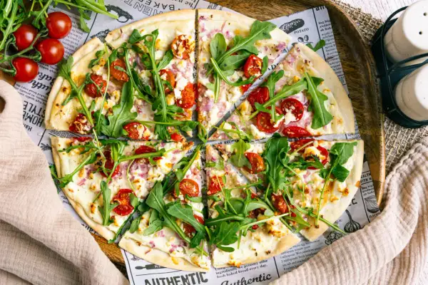 Ein köstlicher flammkuchen vegetarisch mit Kirschtomaten, Rucola und Ziegenkäse auf dünnem Teig.