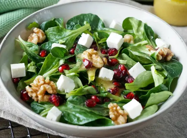 Feldsalat-Rezept: Grüner Salat mit Granatapfelkernen, Walnüssen und Feta-Würfeln, beträufelt mit einem leichten Dressing.