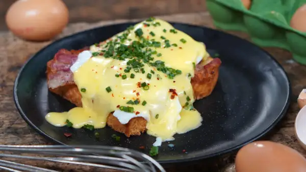 Ein köstliches Egg Benedict mit pochiertem Ei, Speck und Sauce Hollandaise, garniert mit Schnittlauch und Chiliflocken.