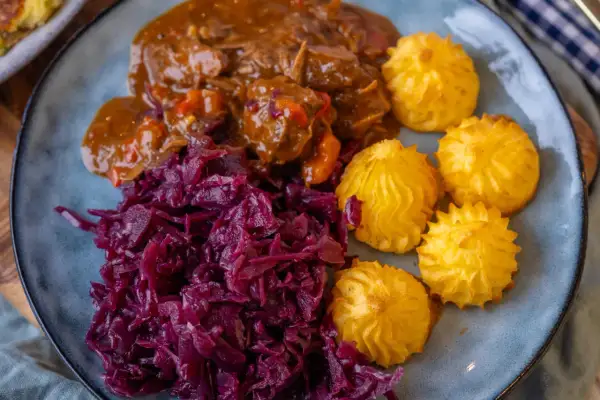 Herzoginkartoffeln selber machen ist einfach! Hier sind sie mit deftigem Gulasch und Rotkohl auf einem Teller angerichtet.